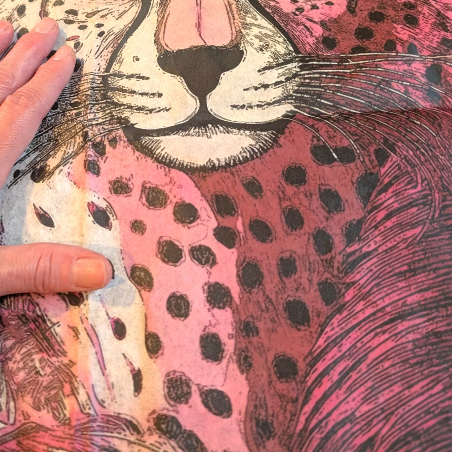 A close-up view of a hand resting on a colorful, patterned fabric with a detailed illustration of a leopard's face.