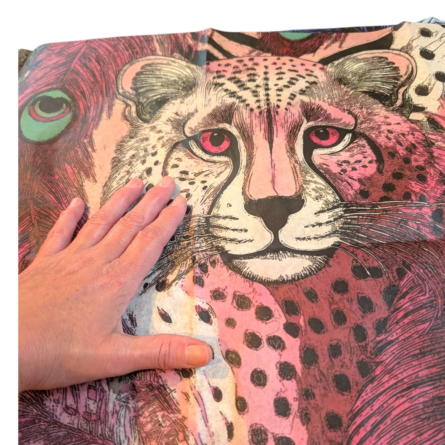 A hand is holding up a colorful, detailed illustration of a cheetah, with its distinctive spotted fur and large eyes.